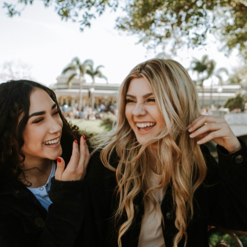 two women laughing outdoors under trees